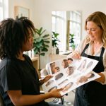Préparer ses cheveux avant un rendez-vous chez le coiffeur Une femme aux cheveux naturels échange avec une coiffeuse dans un salon lumineux en consultant des inspirations de coiffures.