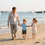 Vacances en famille dans le golfe du Morbihan : le guide pratique Une famille composée d’un homme, d’une femme et de deux enfants se promène sur une plage du golfe du Morbihan, avec des voiliers visibles au loin dans la lumière estivale.